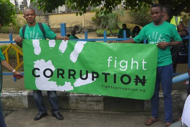 Two men in green with a banner and the text fight corruption