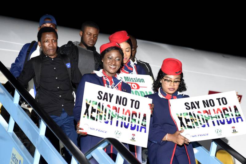 People exiting an airplane carrying signs of Say No To Xenophobia
